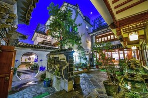 An indoor courtyard with stone flooring, potted plants, and traditional architecture.