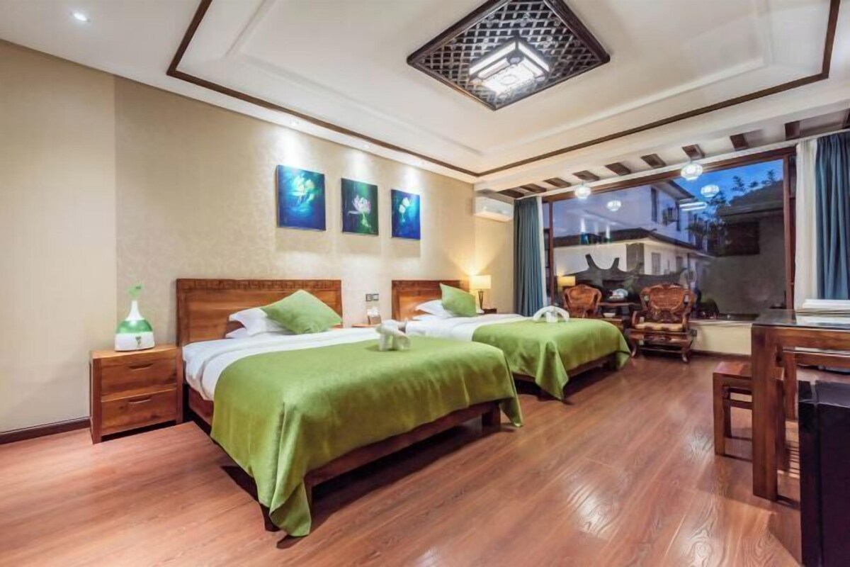 A hotel room with two beds, wooden flooring, a ceiling light fixture, and artwork on the wall.
