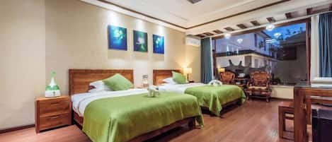 A hotel room with two beds, wooden flooring, a ceiling light fixture, and artwork on the wall.