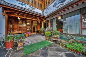 A traditional wooden building with a tiled roof, a stone-paved courtyard, and potted plants.