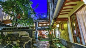 A traditional courtyard with stone flooring, potted plants, and a wooden structure with a balcony. - Qianbaidu Boutique Inn (Dali City)
