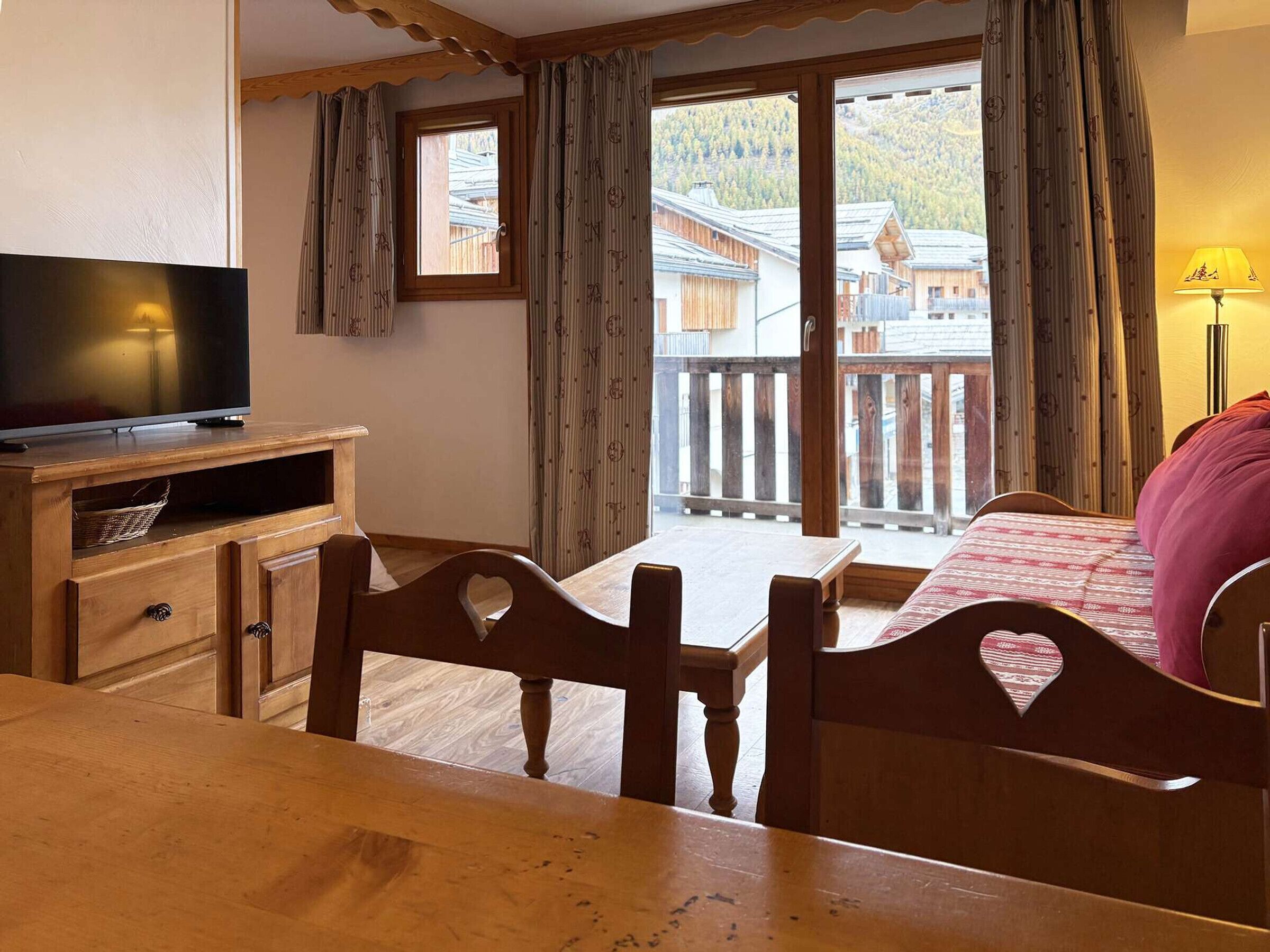 A cozy room with a wooden table, chairs, a TV, and a bed with a red blanket.