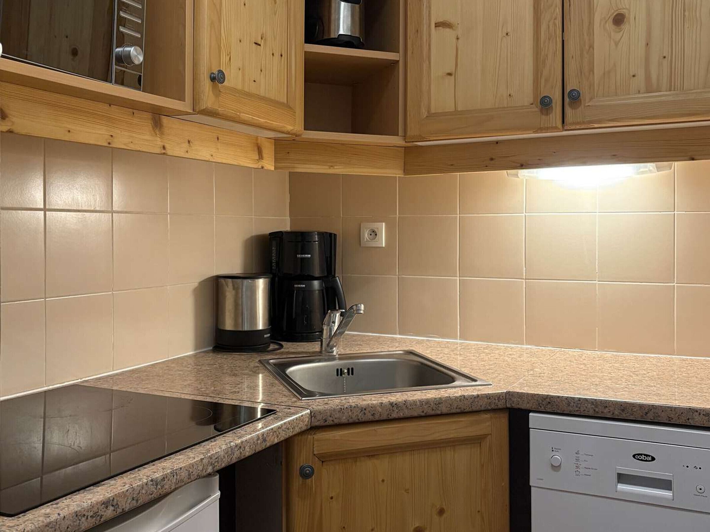 Een keuken met houten kastjes, een RVS-spoelbak, een koffiezetapparaat en een vaatwasser.