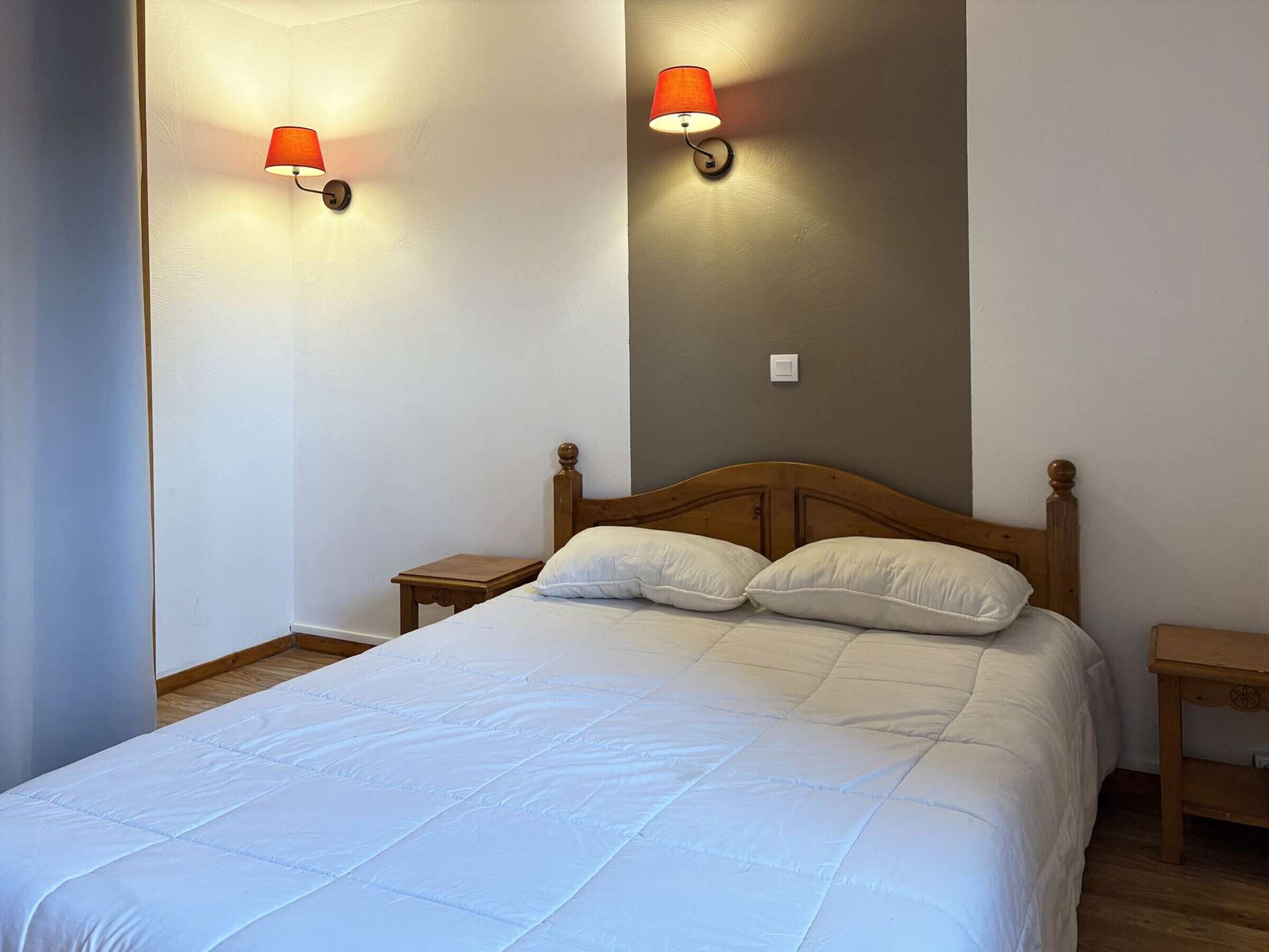 Ein Schlafzimmer mit einem hölzernen Bett, zwei Nachttischen und zwei Wandleuchten.