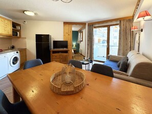 A compact living space with a dining table, chairs, a sofa, a television, a washing machine, and a kitchenette. - Cozy 2-room, sleeps 6, heated pool, sauna, ski-in/ski-out - Les Orres 1800 (Les Orres)