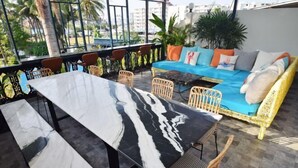 Una terrazza con tavolo in marmo, sedie in vimini, un divano con cuscini e piante in vaso.