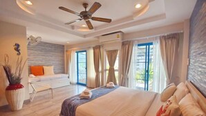 Un'ampia camera da letto con un letto grande, un ventilatore a soffitto e vista sull'esterno attraverso ampie finestre.
