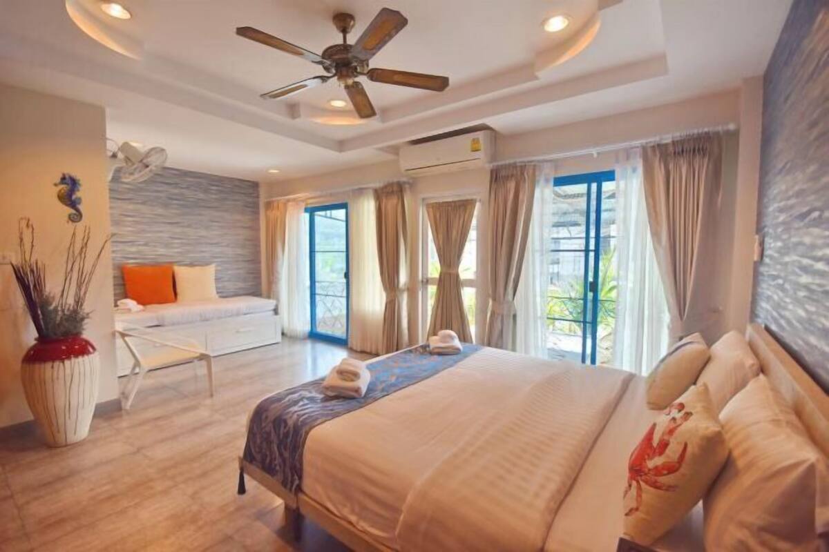 A spacious bedroom with a large bed, a ceiling fan, and a view of the outdoors through large windows.