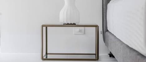 Un dormitorio moderno con una cama tapizada en gris, una mesita de noche blanca con una escultura blanca original y una alfombra estampada en el suelo.