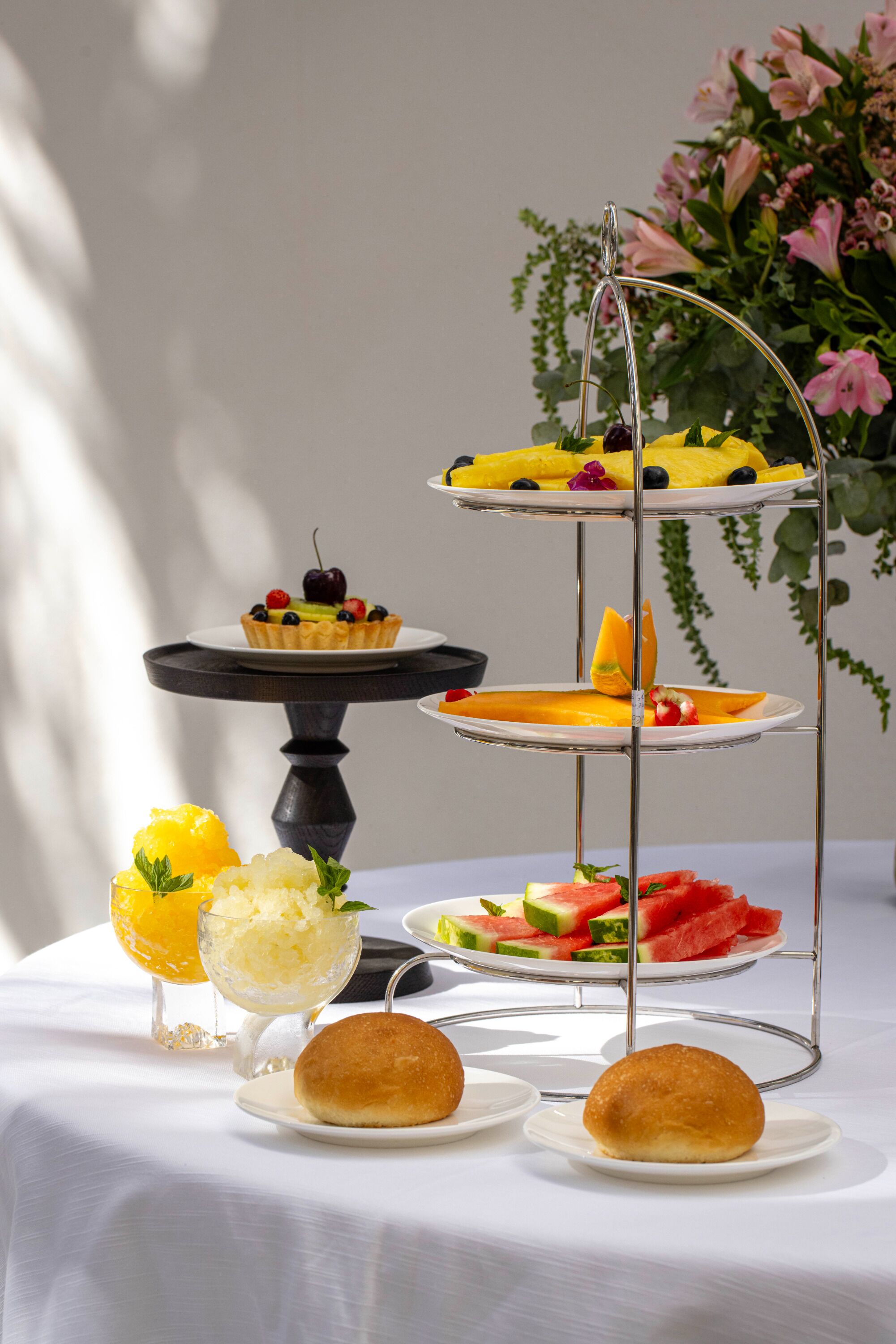 A three-tiered dessert stand with various fruit and pastry items on a white tablecloth.