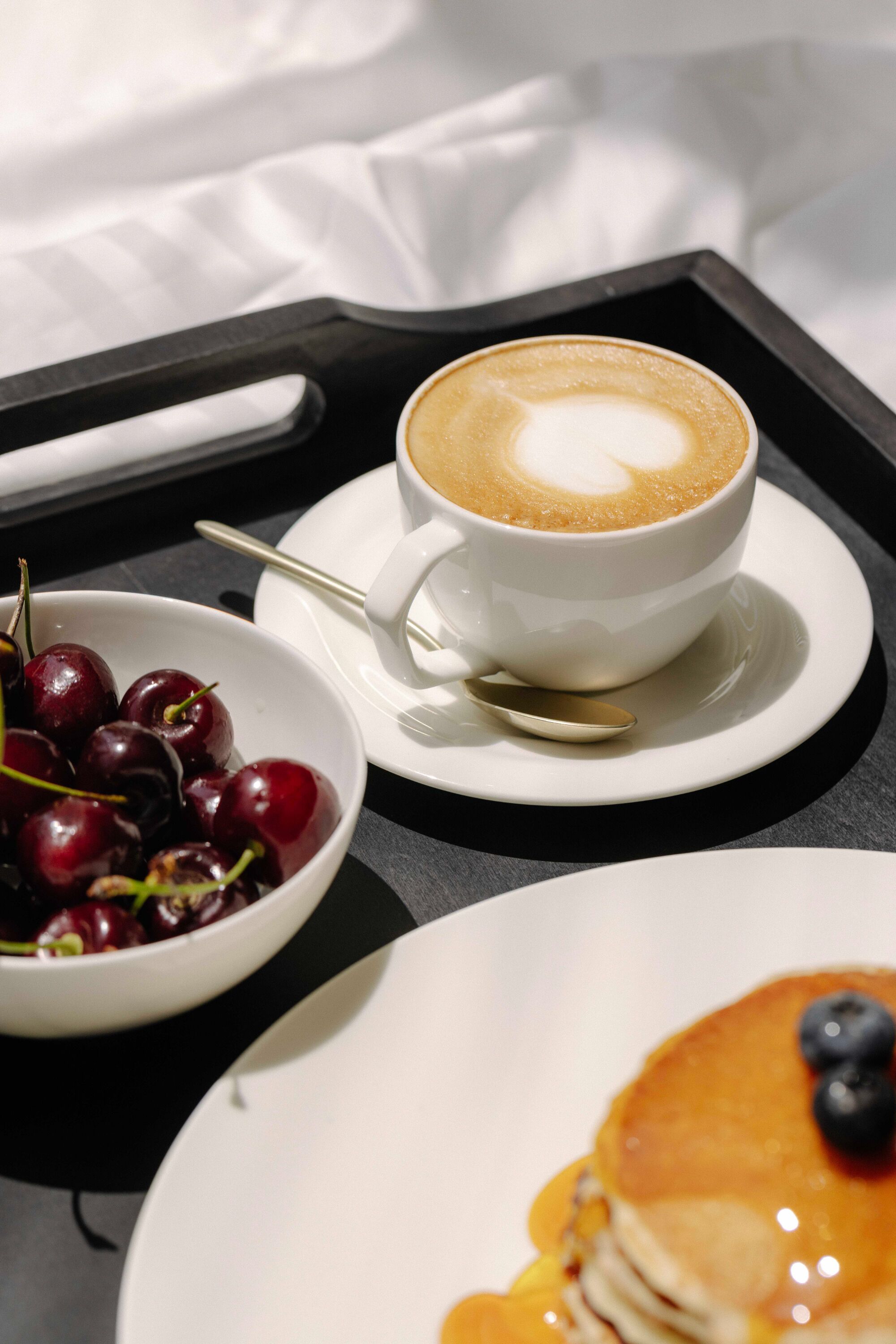 A tray with a cup of coffee, a bowl of cherries, and a plate of pancakes.