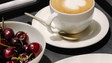 A tray with a cup of coffee, a bowl of cherries, and a plate of pancakes.