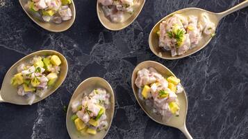Cuatro cucharas sobre una ensalada de mariscos en una superficie de mármol oscuro.