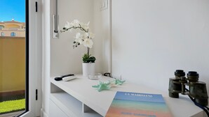 A hotel room with a white desk, a remote control, a book titled "LA MADALENA," and a potted orchid. - Turchesino Apartment (La Maddalena)