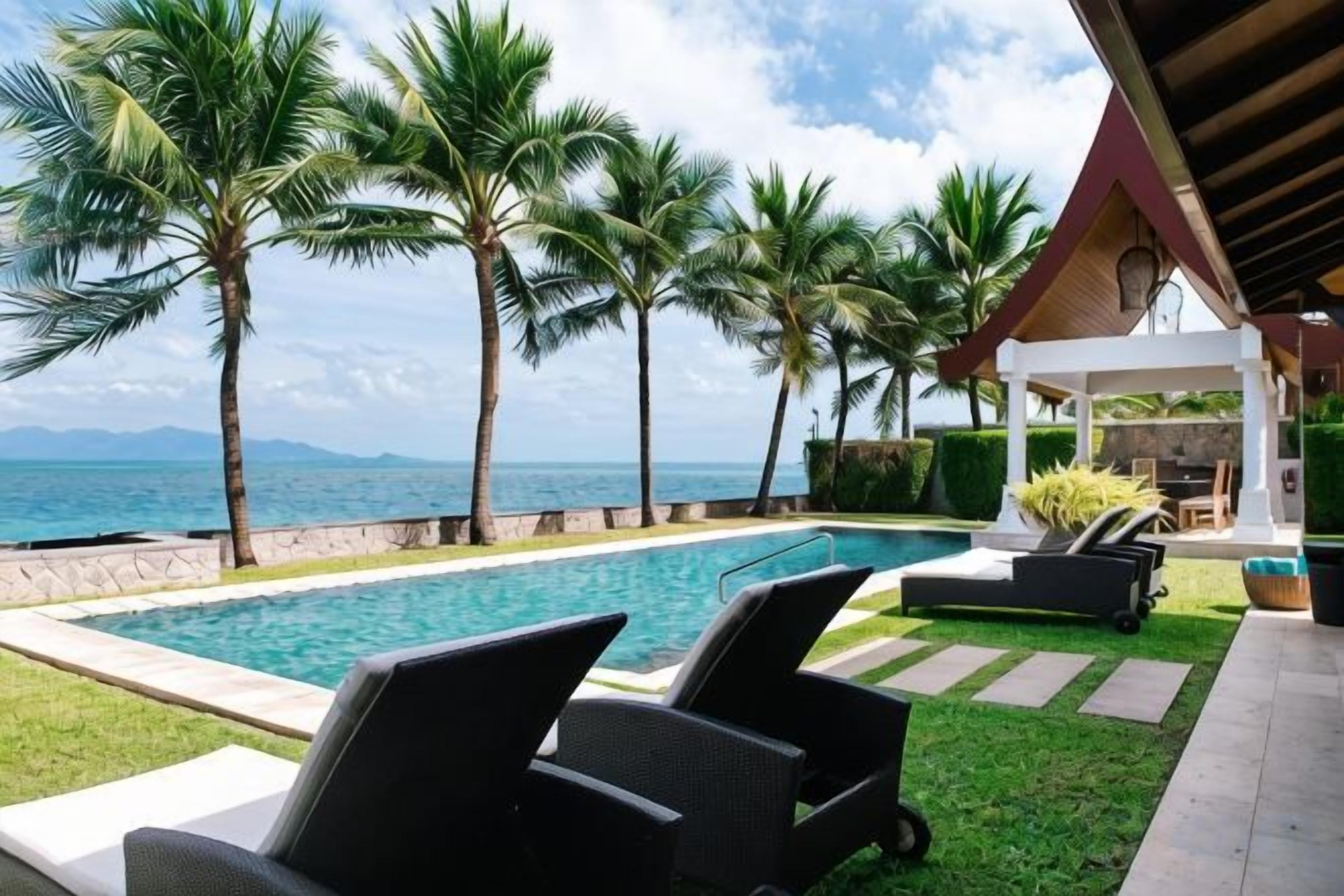 Un área junto a la piscina con sillones de descanso, palmeras y vistas al océano.