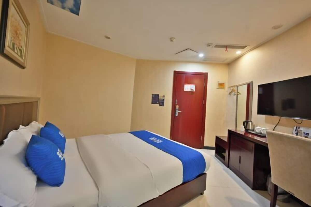 A hotel room with a bed, a desk, a television, and a door.