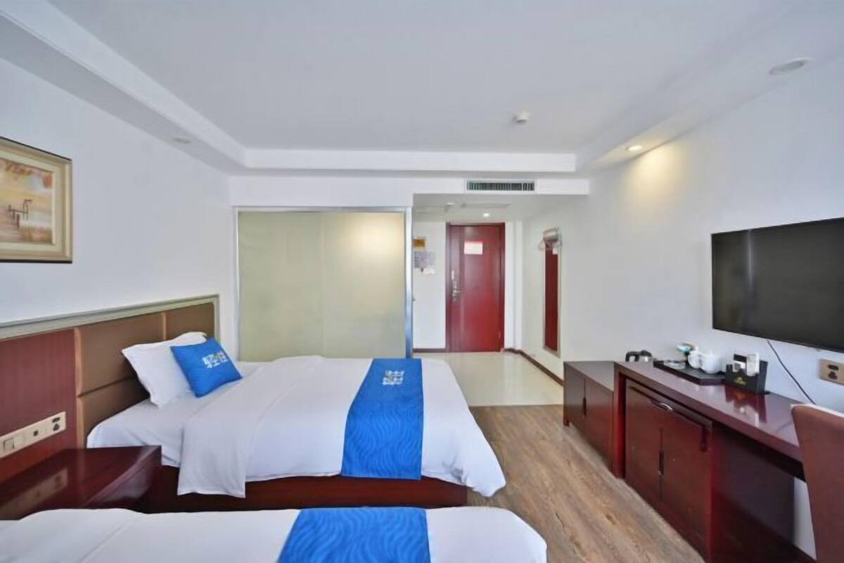 A hotel room with two beds, a desk, a television, and a door leading to another room.