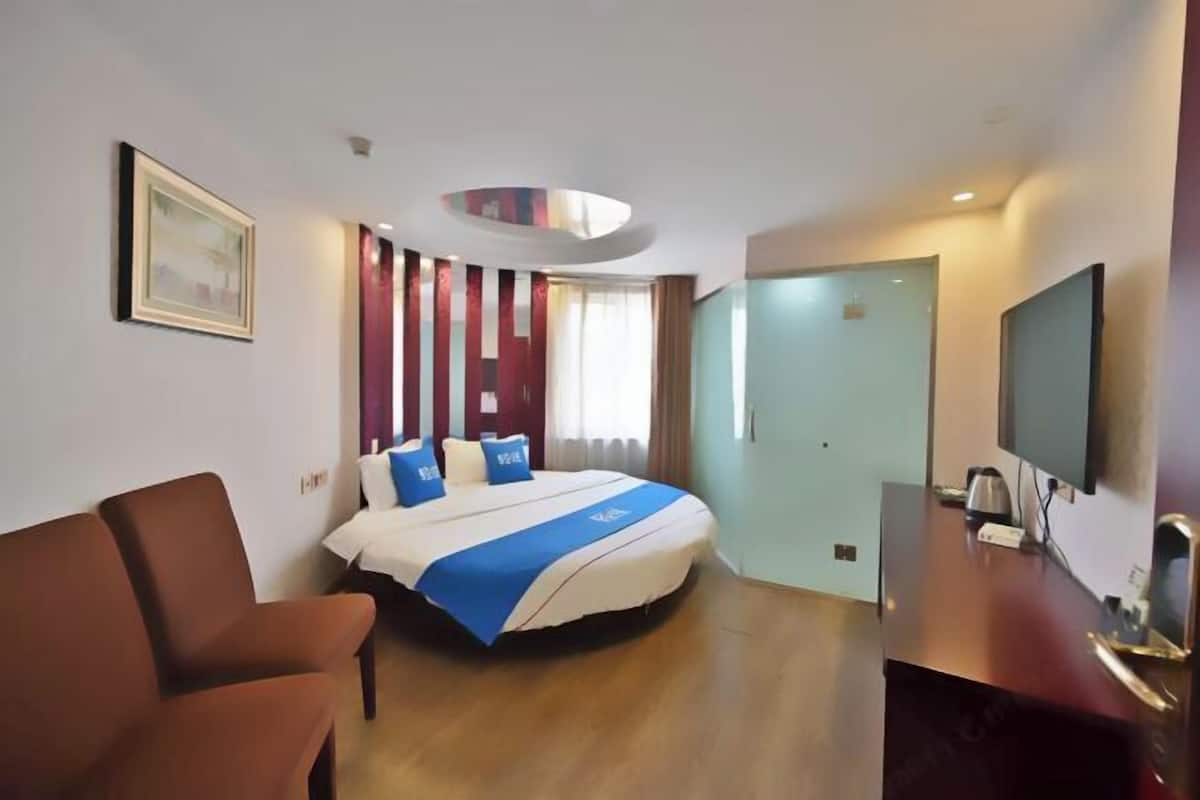 A hotel room with a bed, a desk, a chair, a television, and a door.
