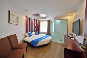 A hotel room with a bed, a desk, a chair, a television, and a door.