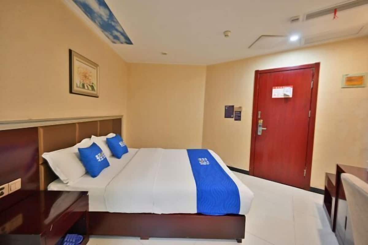 A hotel room with a bed, a wooden headboard, a red door, and a framed picture on the wall.