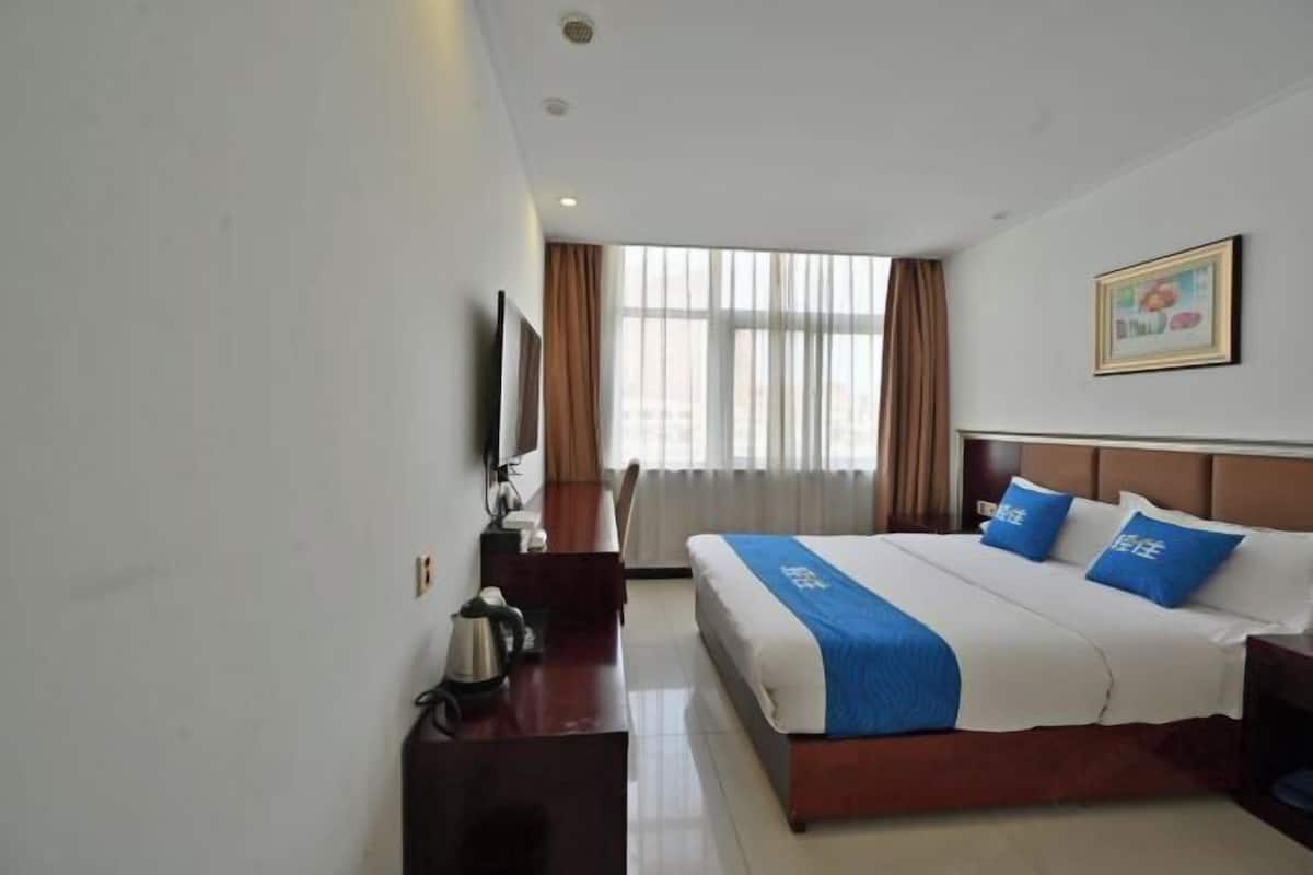 A hotel room with a bed, a desk, a chair, a television, and a window with curtains.