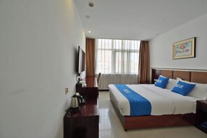 A hotel room with a bed, a desk, a chair, a television, and a window with curtains.