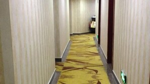 A hotel hallway with striped walls, a patterned carpet, and a door with a green exit sign. - Jinzhai Oriental Business Hotel (Jinzhai)
