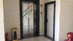 A hallway with a marble floor, a glass elevator, and a closed door. - Jinzhai Oriental Business Hotel (Jinzhai)