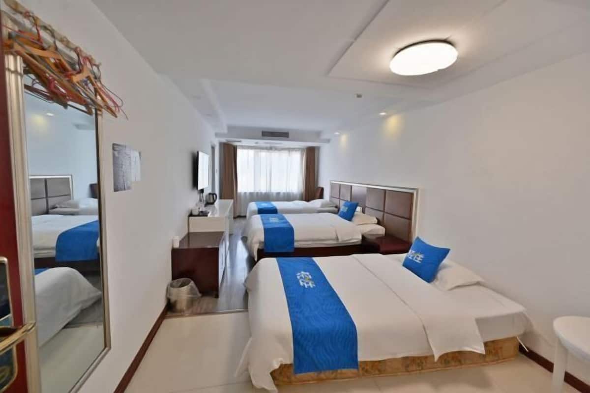 A hotel room with three beds, a desk, a mirror, and a window with curtains.