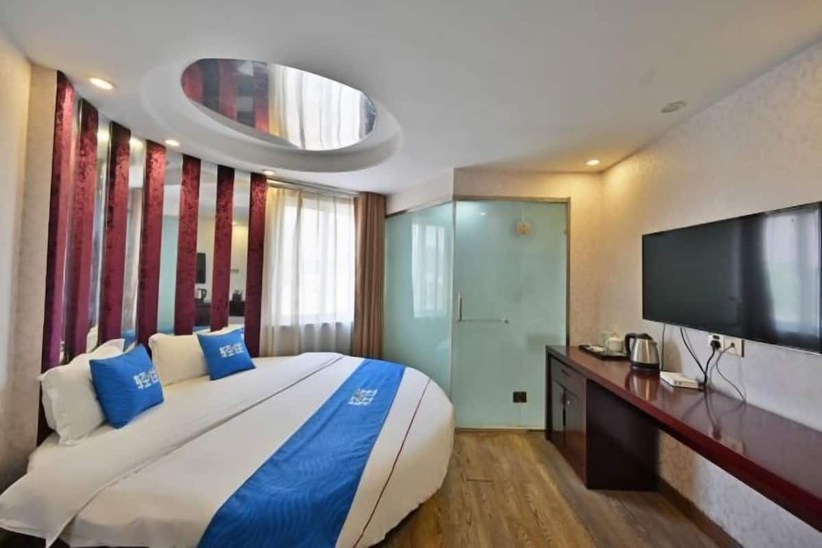 A hotel room with a large bed, a TV, a desk, and a glass door.