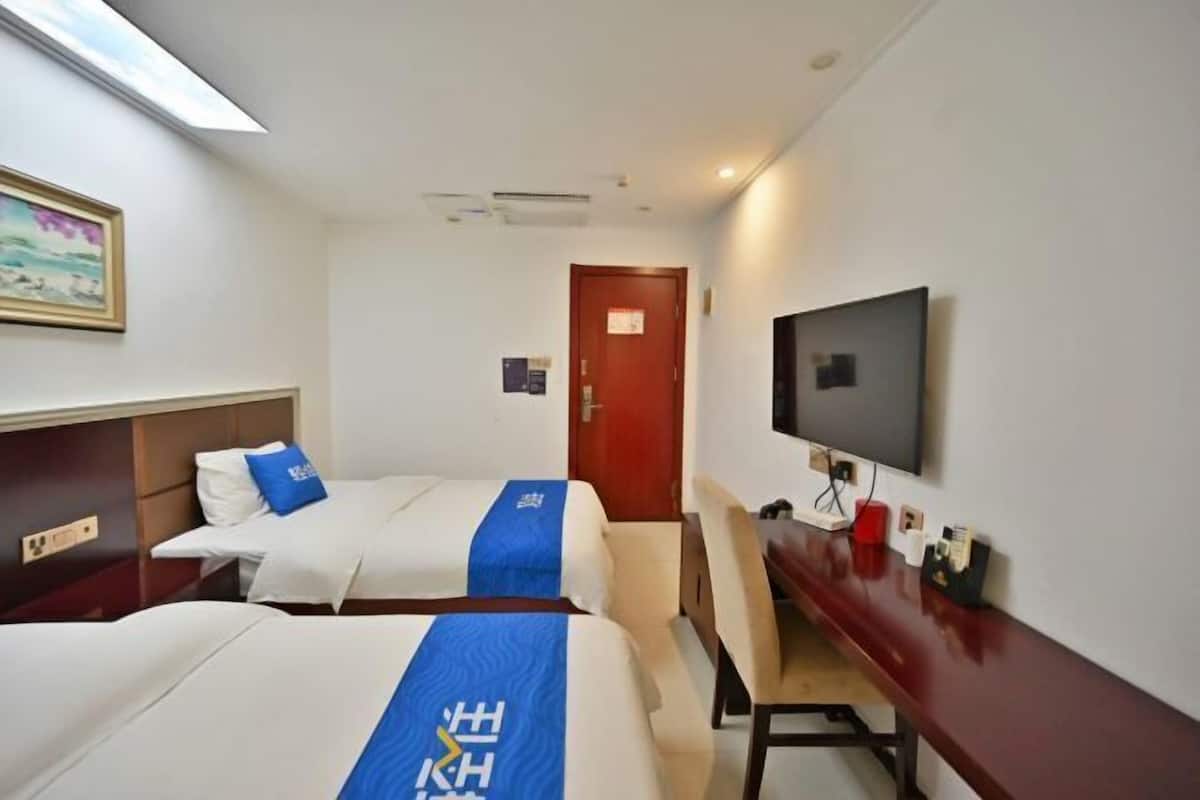 A hotel room with two beds, a desk, a television, and a door.