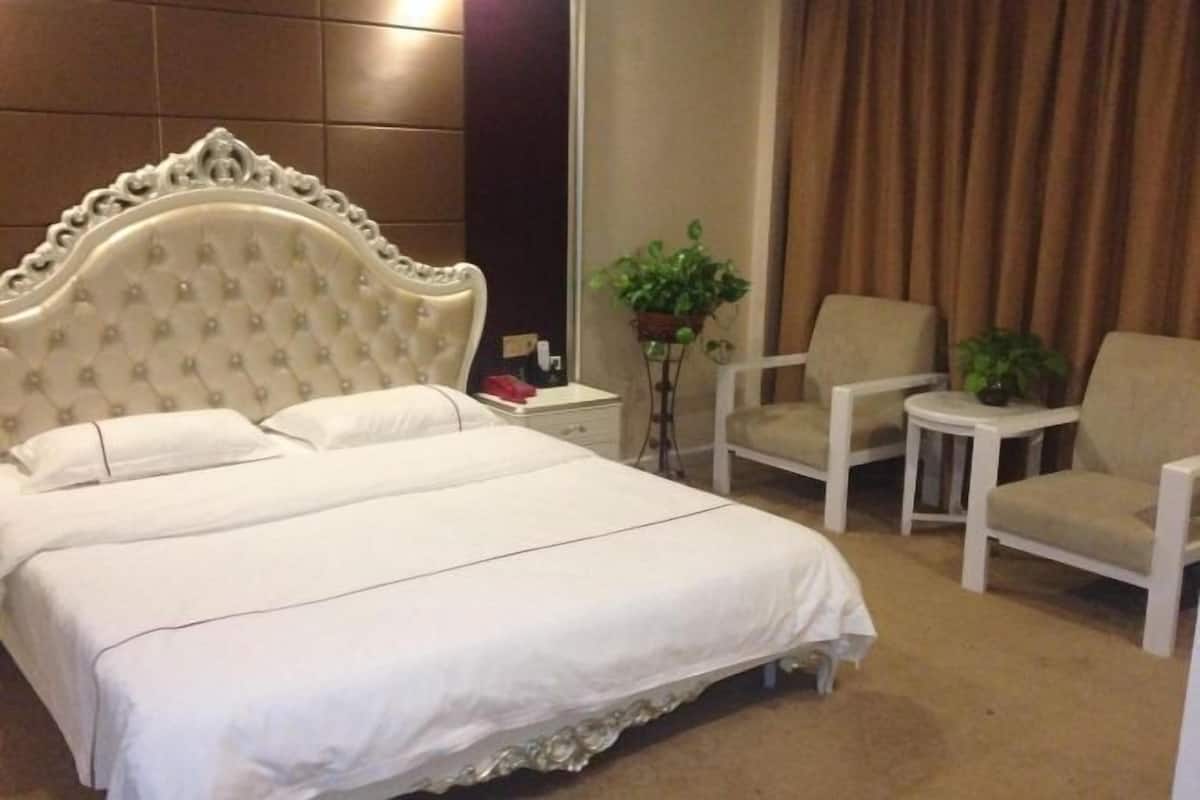 A hotel room with a large bed, two armchairs, a small table, and a potted plant.