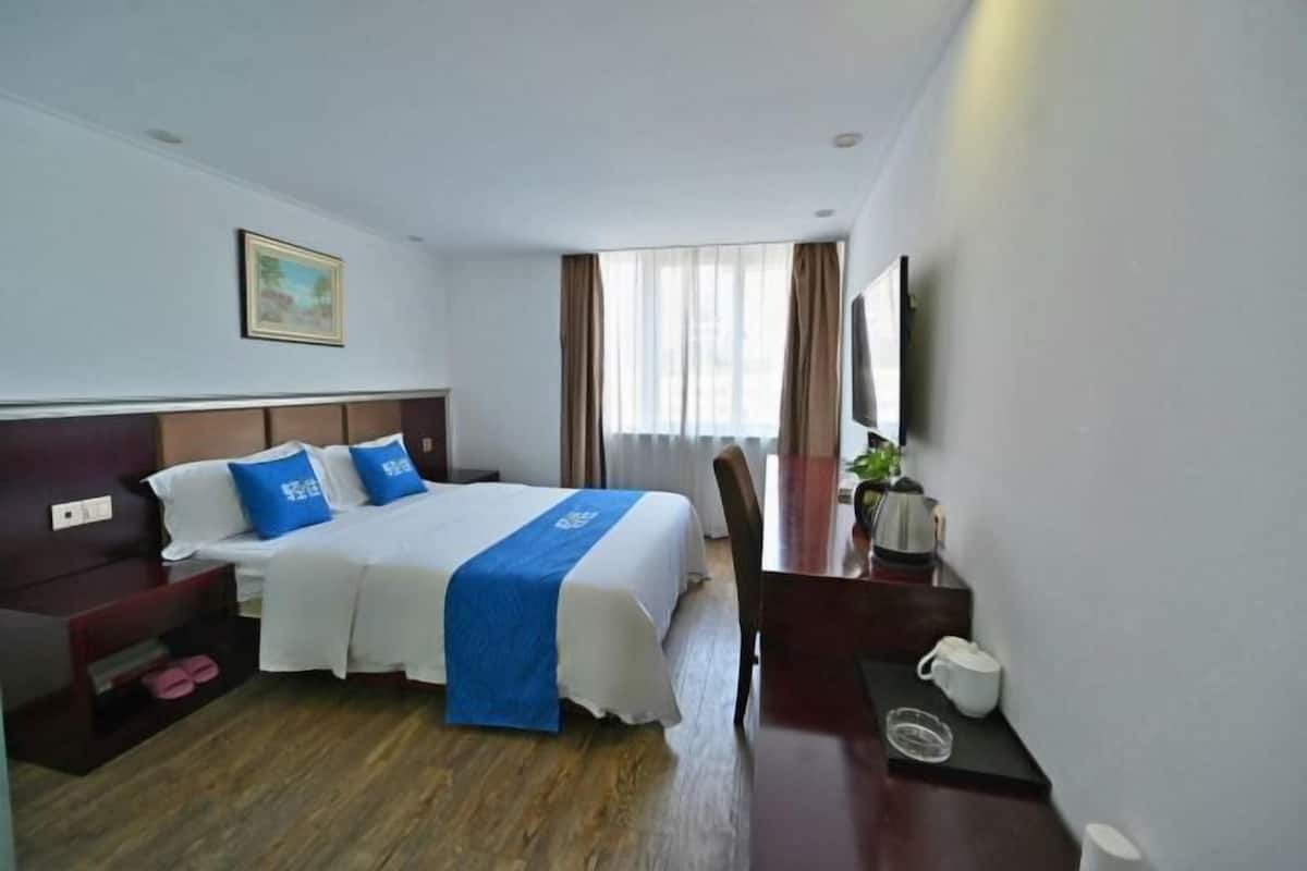 A hotel room with a bed, a desk, a chair, a TV, and a window with curtains.