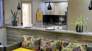 A modern kitchen with granite countertops, a built-in oven, and a sink. There is a dining area with a colorful sofa and a yellow throw blanket.