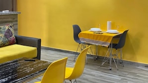 A dining area with a yellow table and chairs, a sofa, and a small table with a glass top.