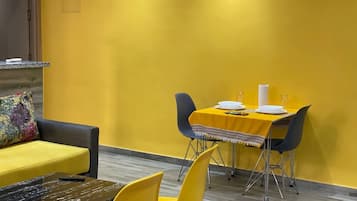 Een eethoek met een gele tafel en stoelen, een bank en een bijzettafeltje met een glazen blad.