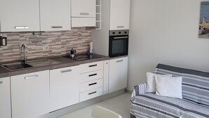 A modern kitchen with white cabinets, a built-in oven, and a dining area with a table and chairs. - Casa Orchidea (Lu Bagnu)