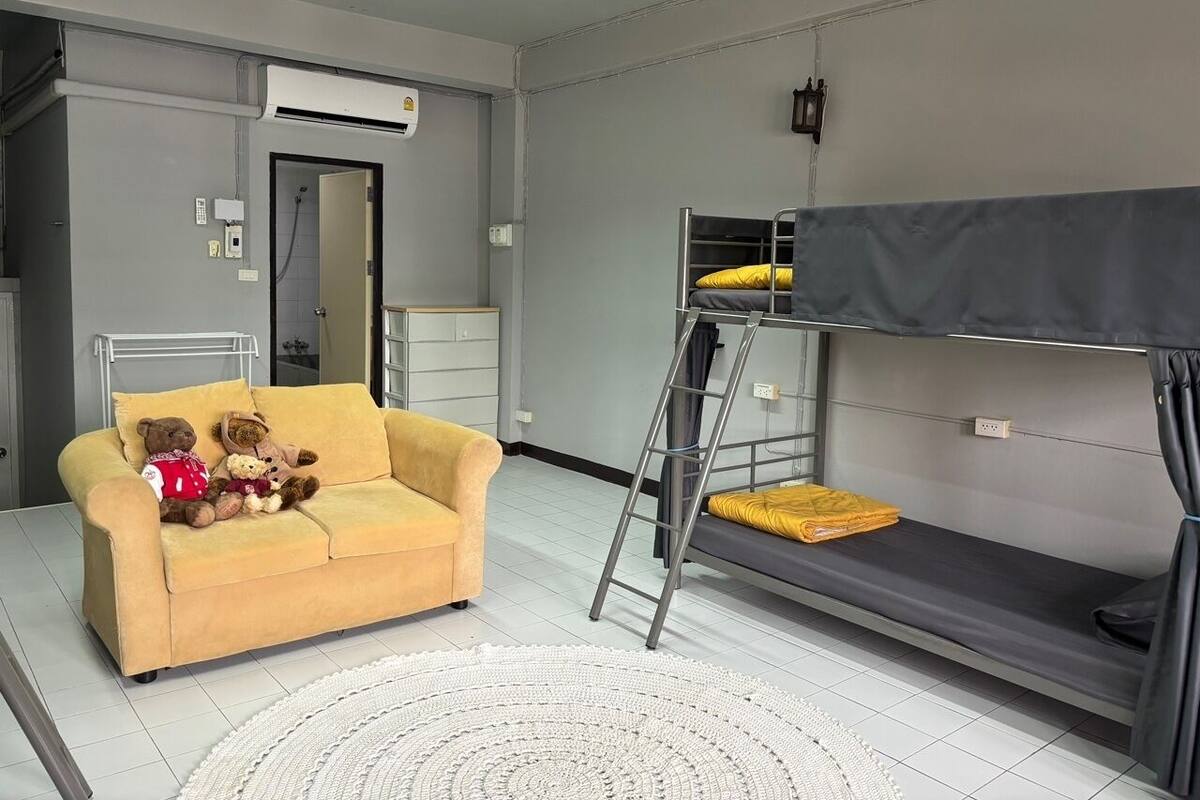 Una habitación con una cama litera, un sofá y un oso de peluche.