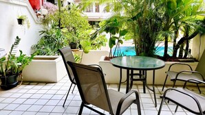 Een terras met een ronde tafel en stoelen, omringd door potplanten en uitzicht op een zwembad.