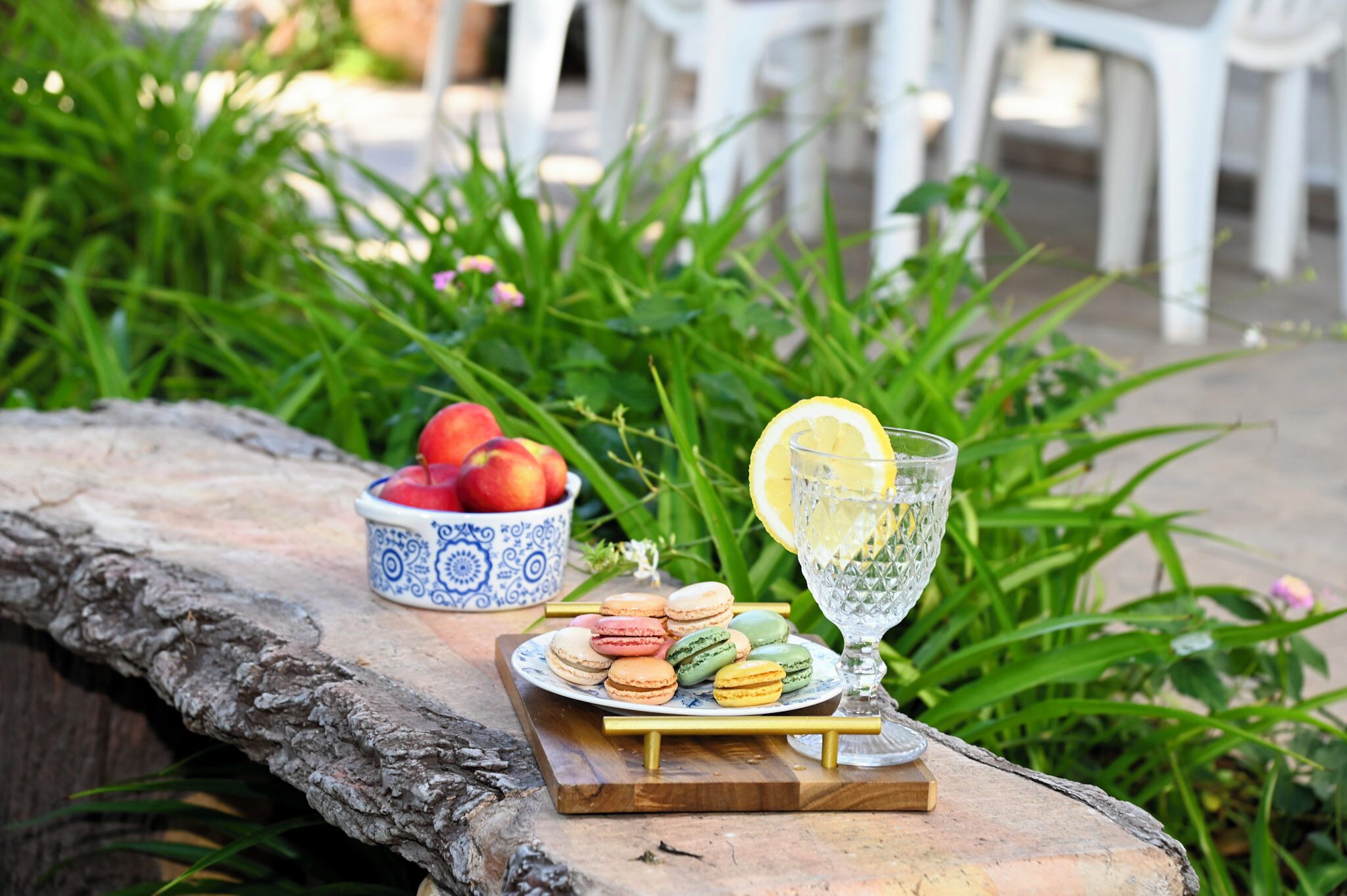 A stone table with a plate of colorful macarons, a bowl of red fruits, and a glass with a lemon slice.