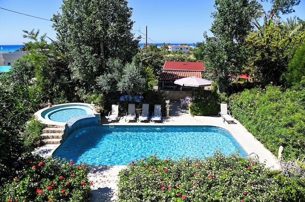 A swimming pool with a hot tub, lounge chairs, and a view of the sea. - Room-kritos Apartments-one Bedroom (Argaka)