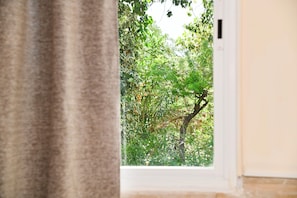 A window with a view of dense green foliage outside. - Room-kritos Apartments-one Bedroom (Argaka)