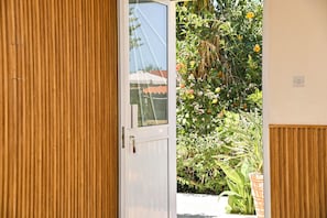 A wooden door leading to a garden with various plants and flowers. - Room-kritos Apartments-one Bedroom (Argaka)