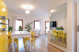 Una sala de estar moderna con comedor, que presenta una gran mesa blanca, sillas amarillas, un televisor y un espejo grande.