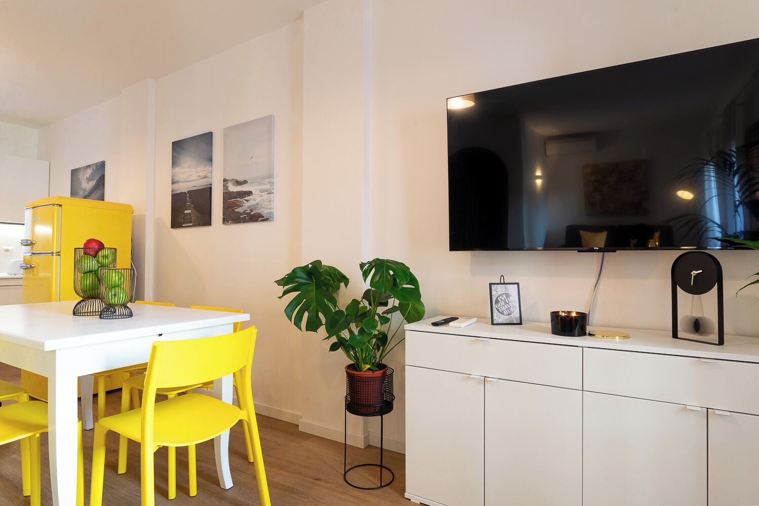 Una cocina moderna con encimera blanca, sillas amarillas, un refrigerador amarillo y un televisor de pantalla plana grande montado sobre la encimera.