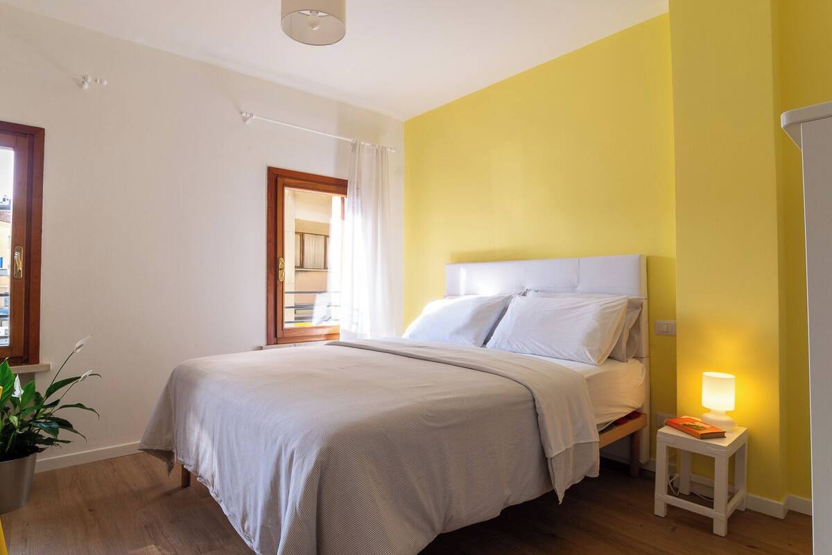 A bedroom with a bed, bedside table, lamp, and a potted plant.