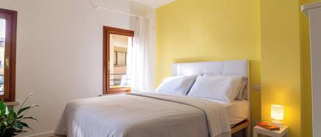 A bedroom with a bed, bedside table, lamp, and a potted plant.