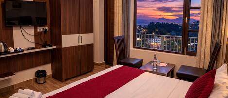 A hotel room with a bed, a TV, a wardrobe, a desk, a chair, and a window with a city view.