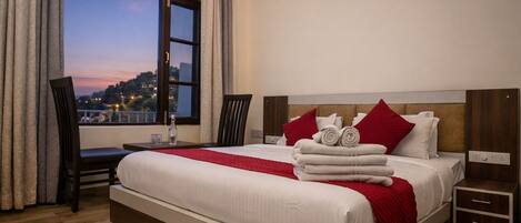 Habitación de hotel con una cama grande, vistas a un paisaje urbano, un escritorio con silla y una mesita de noche.