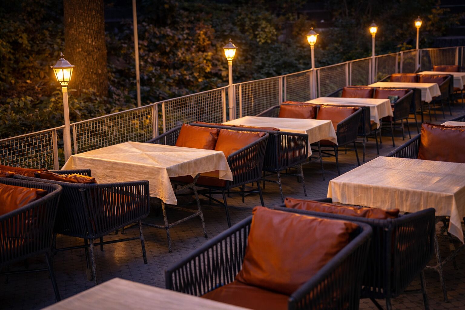 An outdoor dining area with tables and chairs, surrounded by a railing and trees.